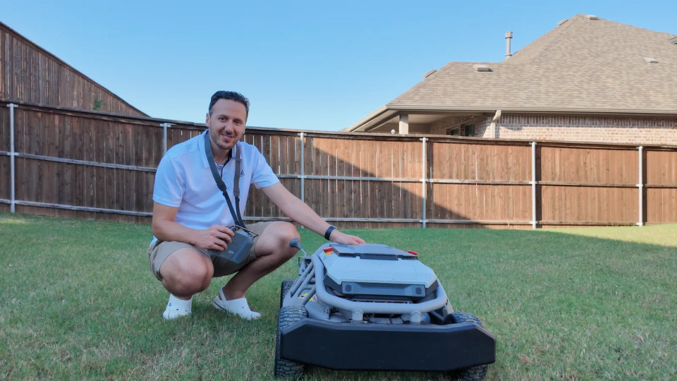 Man kneeling on grass holds remote and touches Mowrator robotic lawn mower in backyard