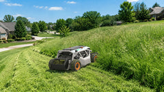 The Mowrator cuts through thick, overgrown grass on a wide slope, leaving clear mown lines in a suburban yard