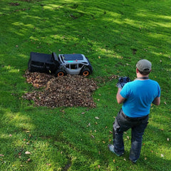 Mowrator remote-controlled leaf vacuum collects pile of brown leaves on sunny grassy lawn with operator holding remote