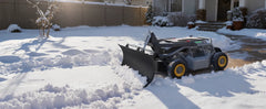 Mowrator remote control snow plow with yellow wheels and black blade clearing residential driveway snow