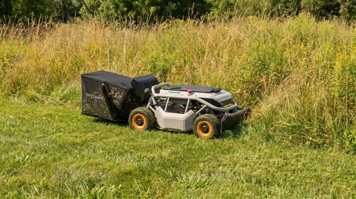 Mowrator remote control mower with a grass bag cutting beside tall field grass and weeds